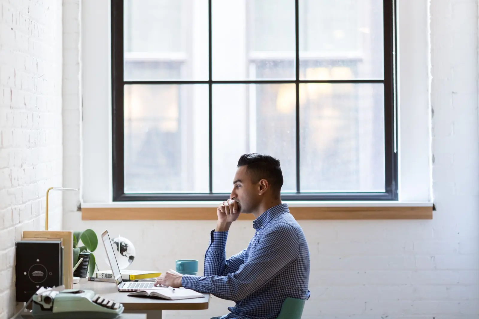 A professional working on a laptop at a desk beside a large window
