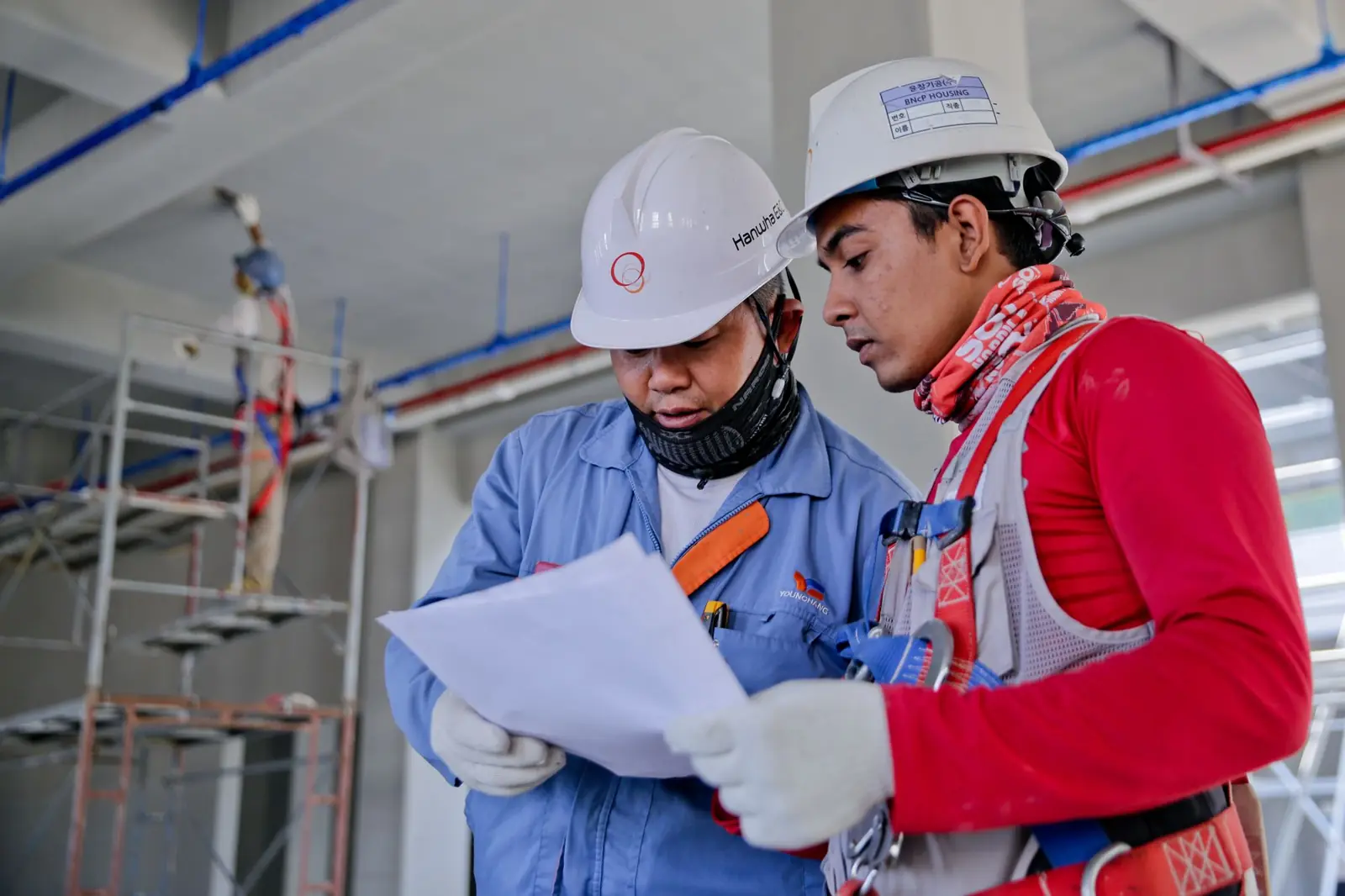 Two engineers in safety helmets reviewing plans at a work site