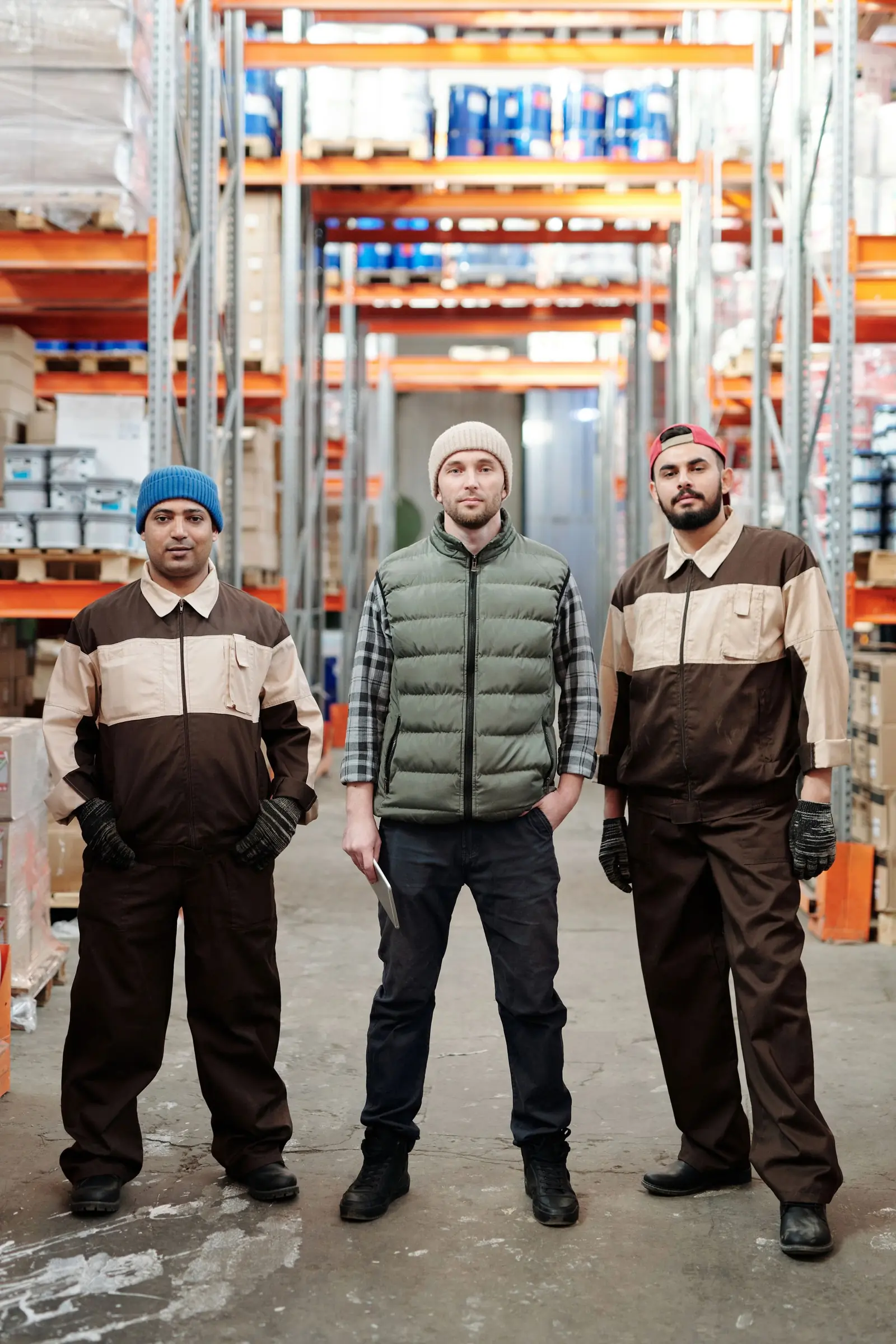 Three warehouse team members in uniform standing between stocked shelves